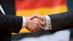 Two people shaking hands in front of a German flag 