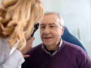 An elderly man receiving a comprehensive eye examination from a female optometrist using an ophthalmoscope.