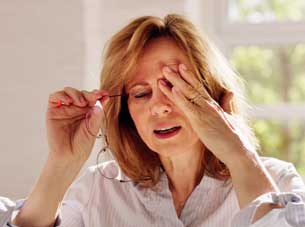 A woman holding her eyeglasses and rubbing her eyes, appearing to suffer from eye strain or dry eye symptoms.