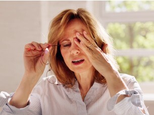 Woman holding eyeglasses and rubbing her eyes, appearing to experience eye strain or discomfort.